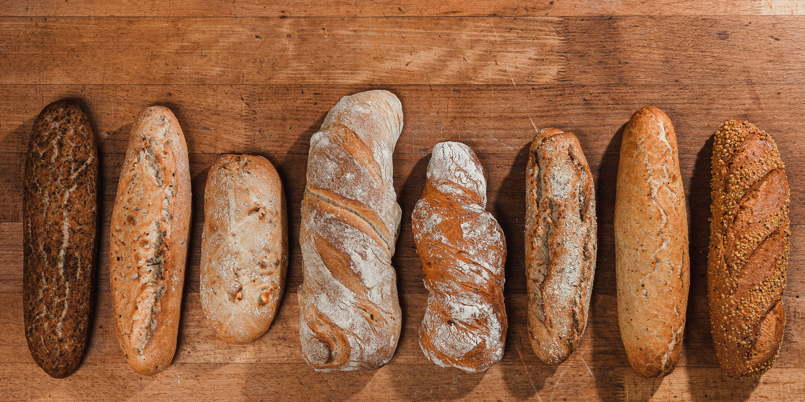 verschiedene Baguette liegen aufgereiht auf einem Holzuntergrund